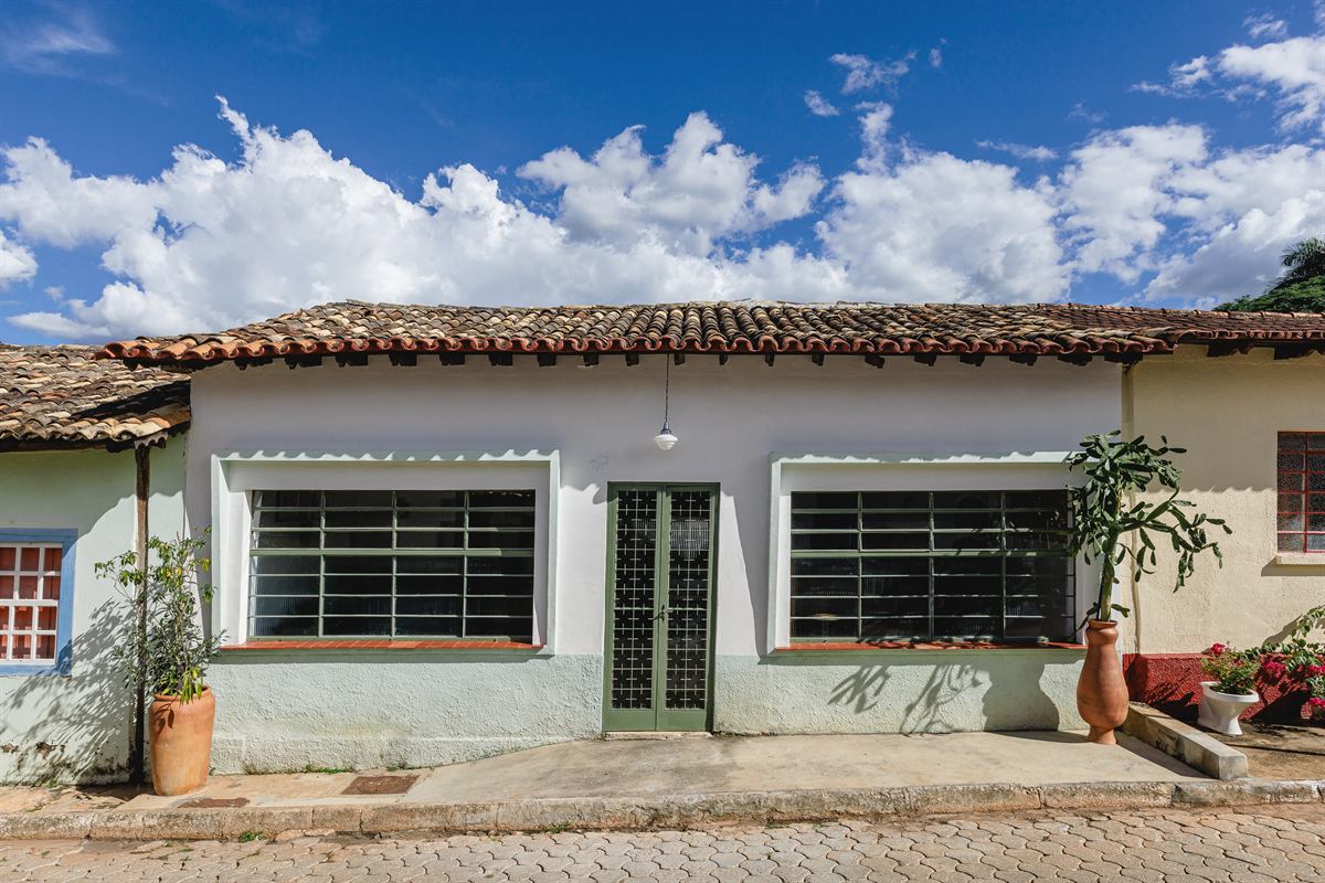 Fachada térrea da Casa Tempo, de paredes brancas, janelas com grade e porta verde, em rua de pedra do centro histórico
