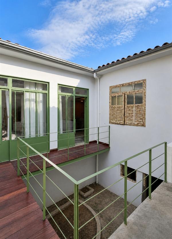 Passarela de madeira com guarda-corpo verde entre as alas da casa