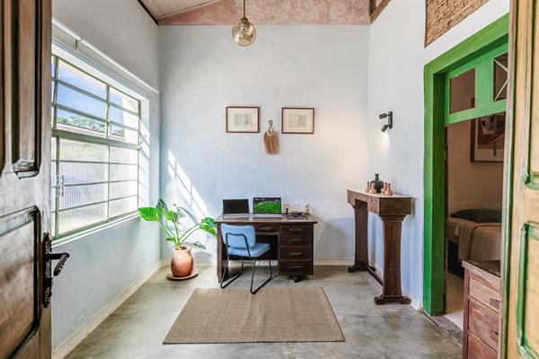 Escritório claro com mesa de trabalho, cadeira, planta e janela de grade