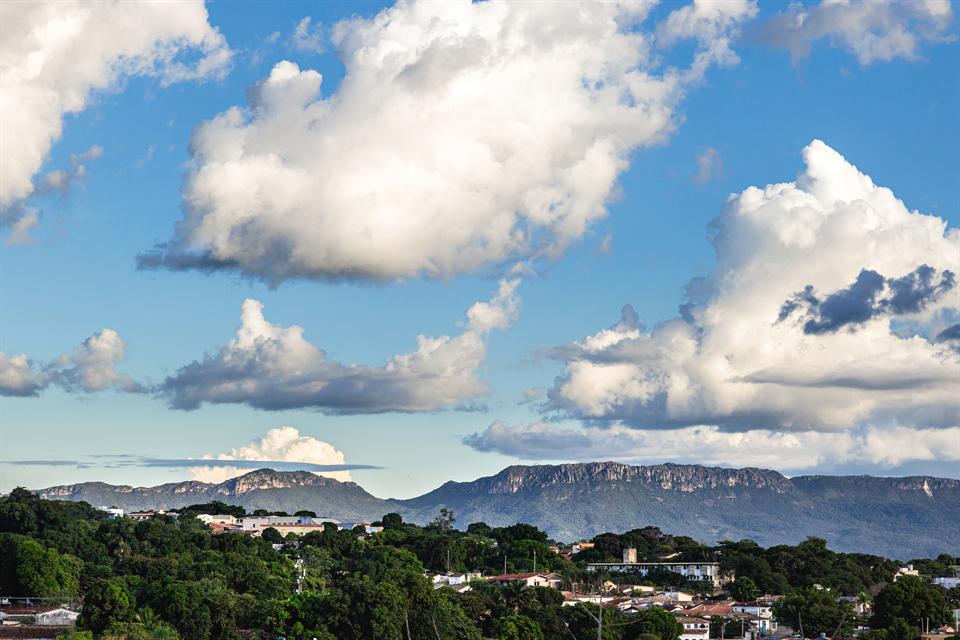 Vista da Serra Dourada sobre a mata e os telhados da cidade, sob céu azul com nuvens