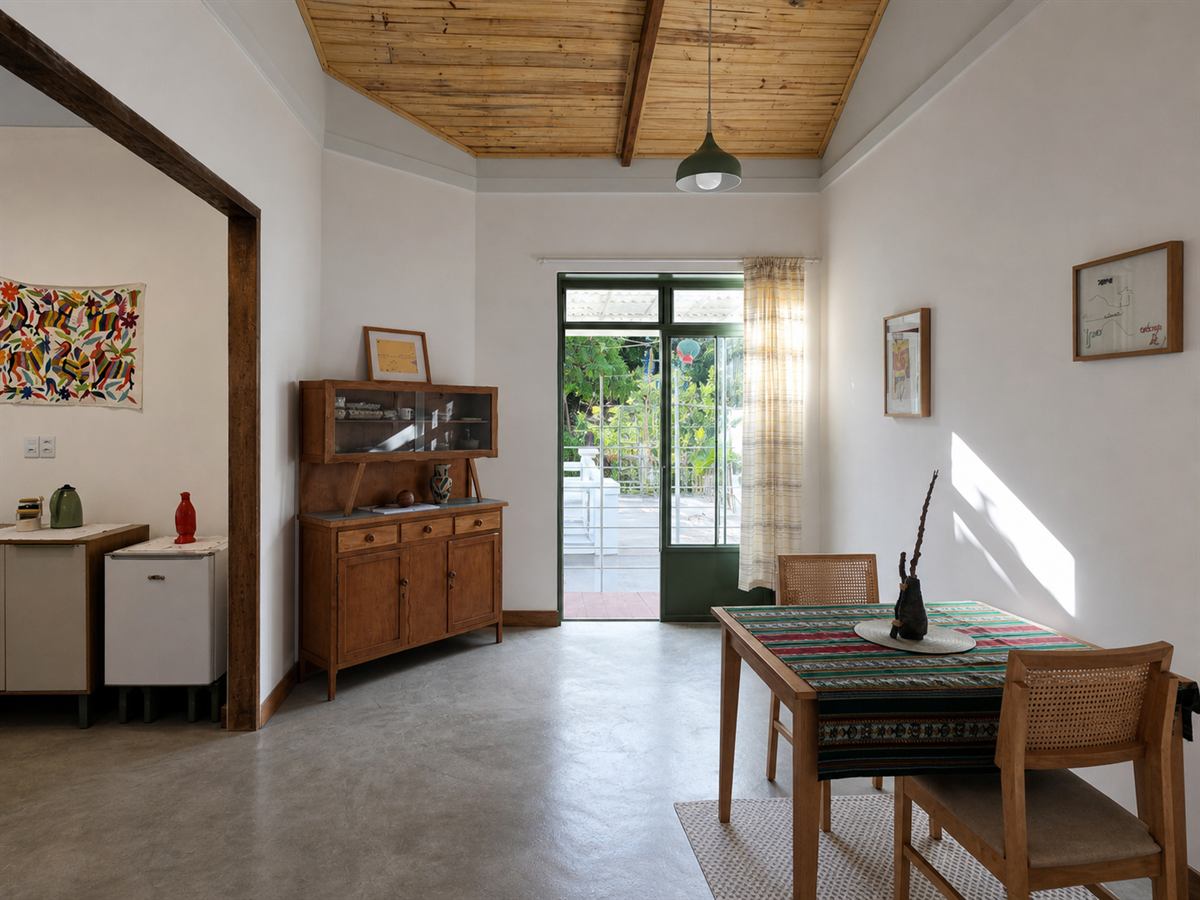 Sala de jantar com mesa de madeira, toalha estampada e porta aberta para o quintal iluminado