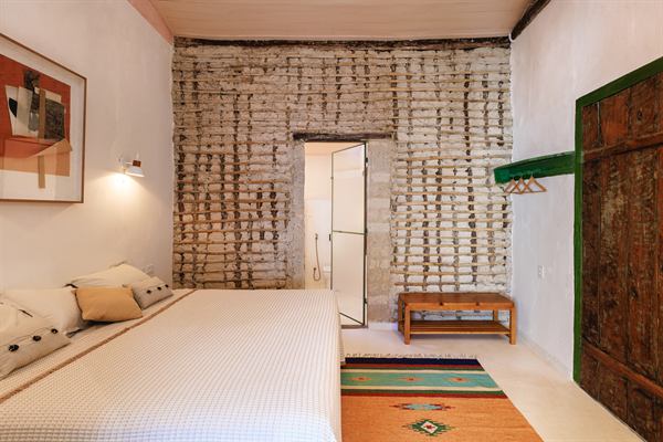 Suíte com cama de casal branca, parede de tijolos caiados e porta de madeira verde