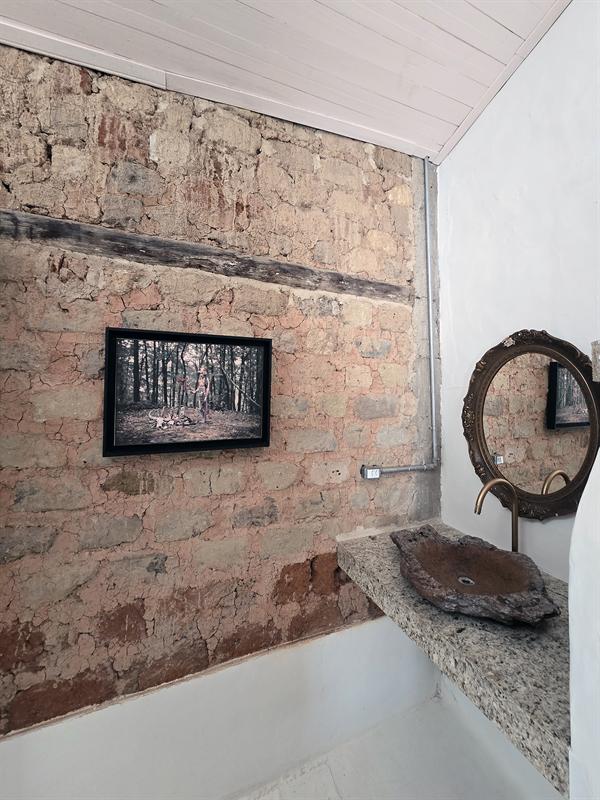 Parede de pedra à vista com quadro, espelho redondo e bancada de pedra