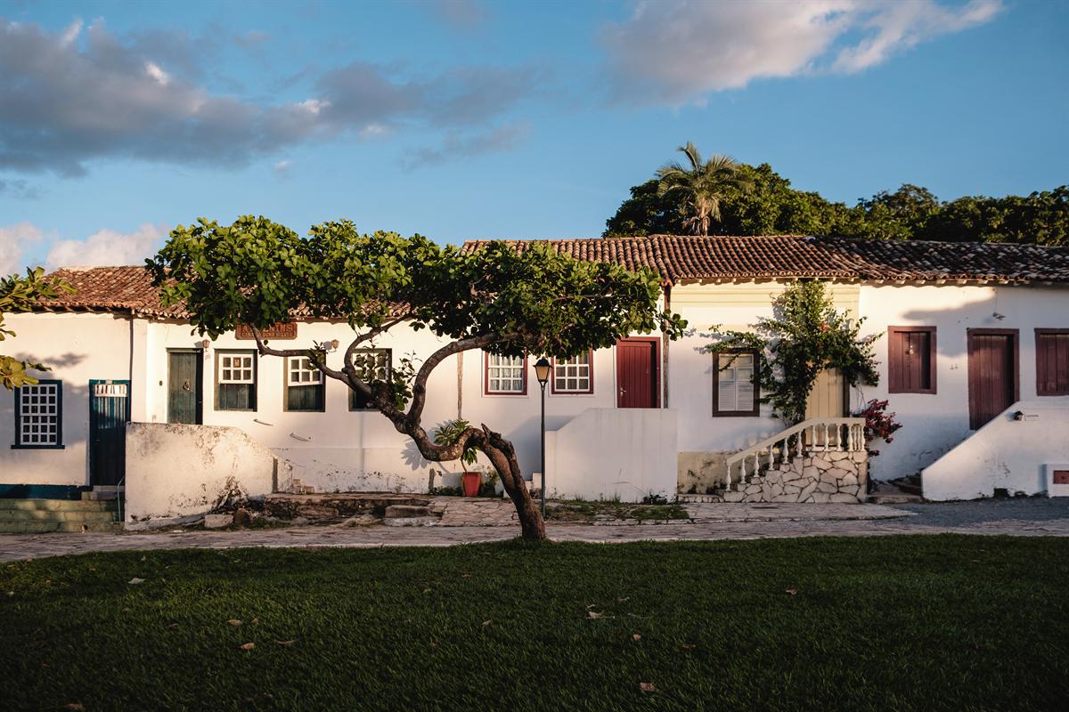 Casario colonial branco de janelas coloridas diante de um gramado com árvore, no centro histórico de Goiás