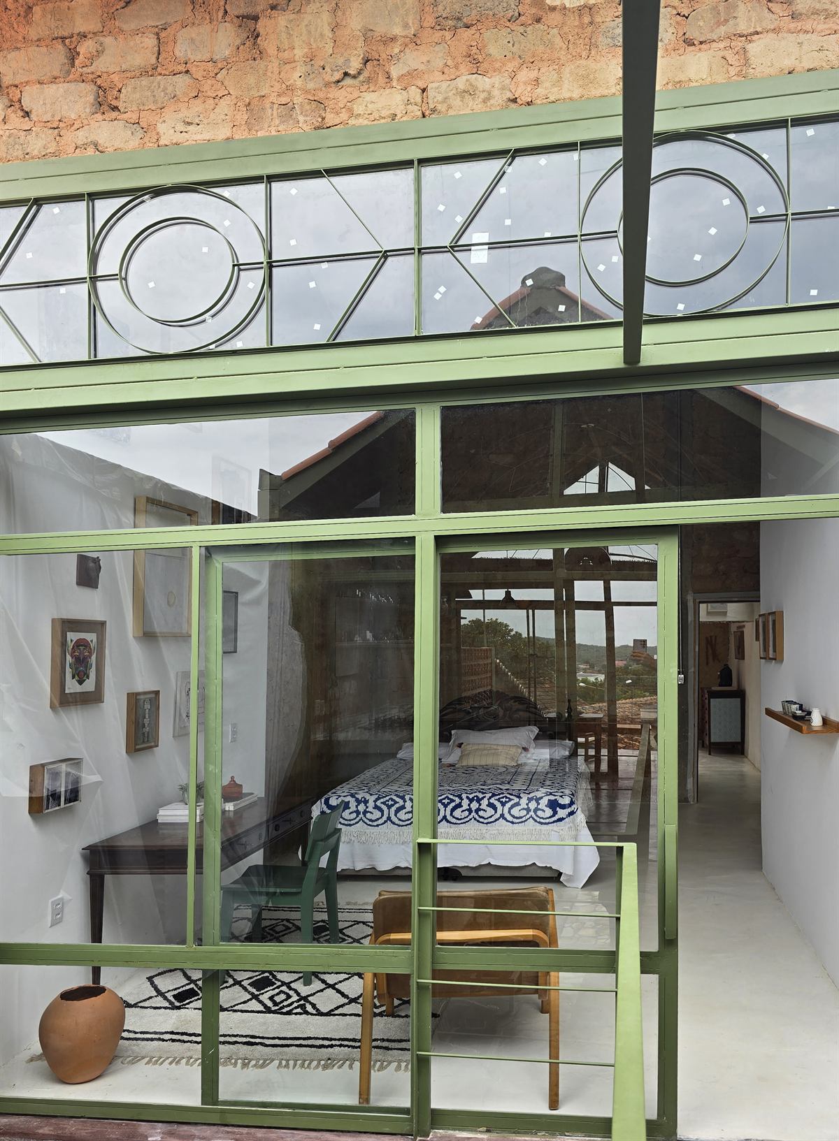 Estrutura de ferro verde com vitrais geométricos diante de parede de pedra antiga